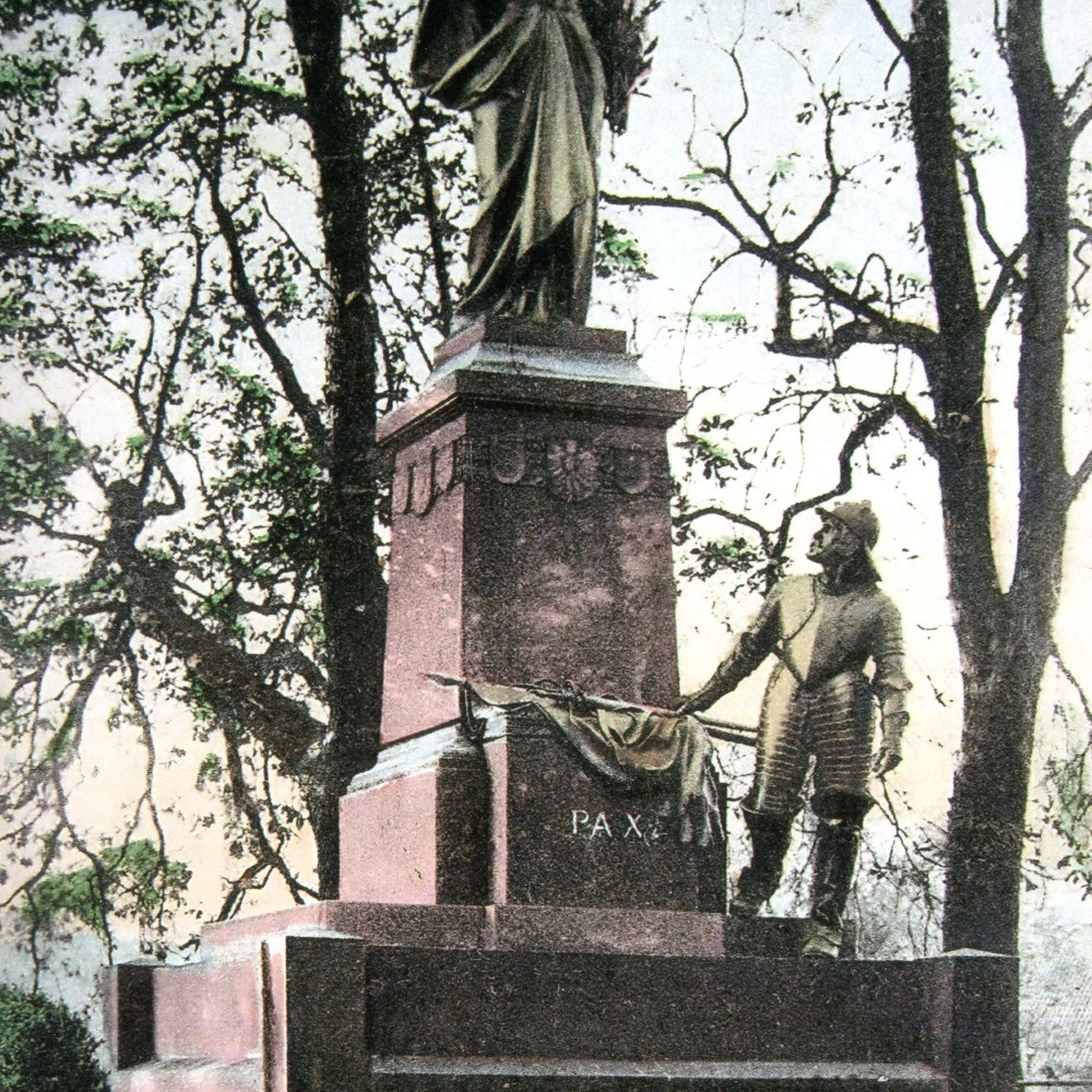 Friedensdenkmal von dem Bildhauer Wilhelm Bolte. Dieses wurde am 01.07.1905 (01.06.1905?) auf der Höhe des Hügels am Kanonengraben eingeweiht. Es war fast 8 m hoch und zeigte eine Frauengestalt als Symbolfigur für den Frieden (Friedensgöttin Pax). Das Denkmal sollte an den Westfälischen Frieden von 1648 erinnern. Es wurde aufgrund der Metallknappheit während des Zweiten Weltkriegs teilweise abgebaut und später gänzlich demontiert (zuletzt 1954). Zeitgenössische Ansichtskarte. Siehe hierzu: H. Metzler, Ein denkmal des Westfälischen Friedens, in: Westfalenspiegel, Heft 2, 1995, S. 21 - 22.